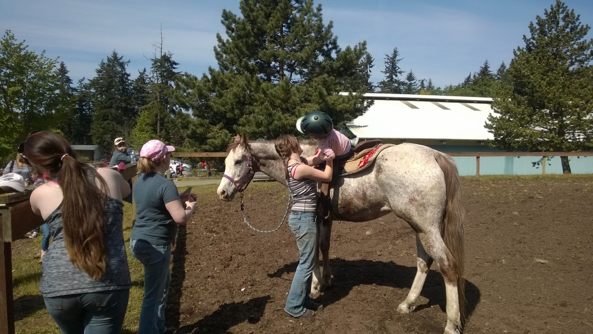 Child helped onto horse in outdoor arena